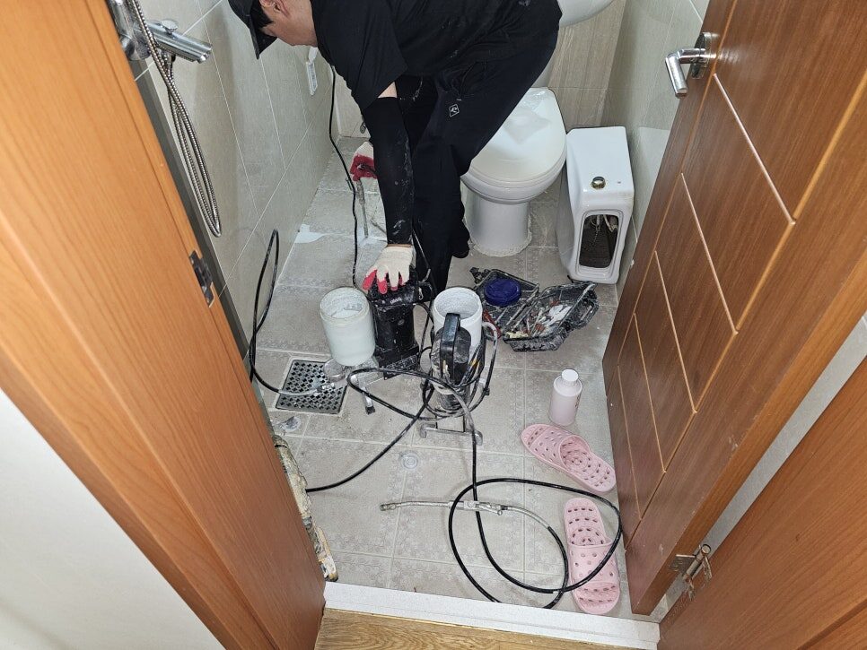 욕실 바닥에서 타일을 철거하지 않고 주입 장비와 호스로 작업 중인 기술자